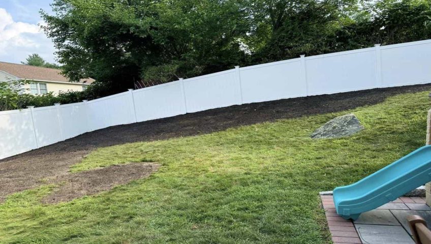 White vinyl privacy fence installed along a sloped backyard showing seasonal fence installation and property boundary protection for residential landscaping