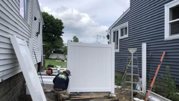 Worker installing a white vinyl fence on uneven ground during fence installation in Massachusetts