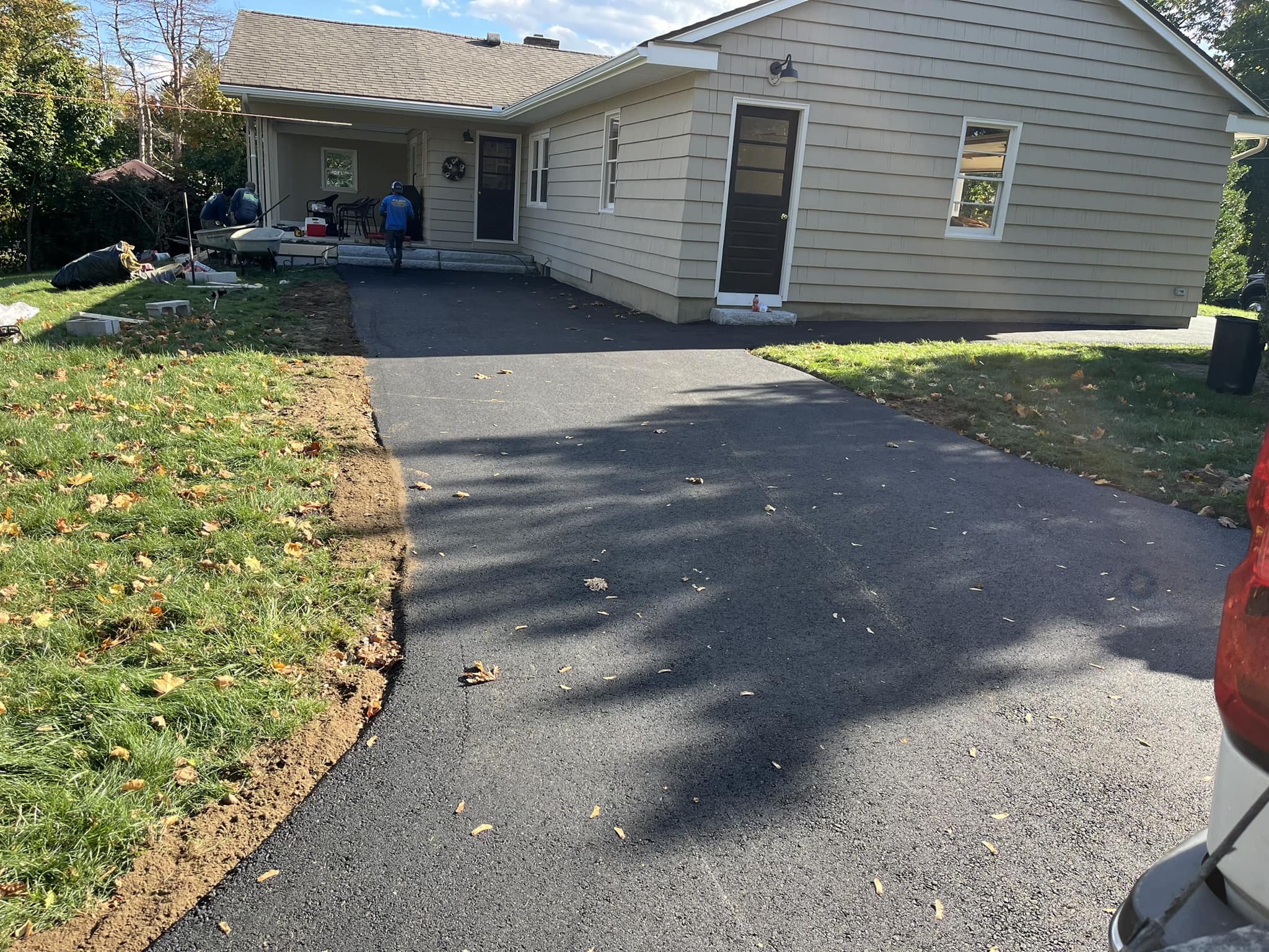 Residential asphalt driveway installation process with fresh blacktop surface and workers preparing the area