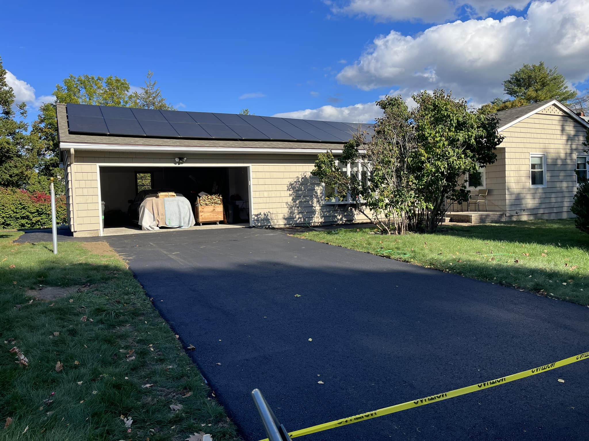 New asphalt driveway installation at a residential home leading to a garage with smooth blacktop finish