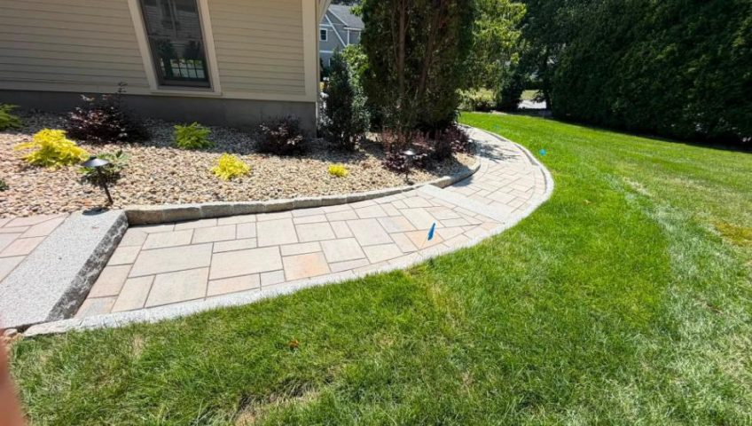 Curved paver garden path bordered by decorative stone landscape beds and a healthy green lawn.