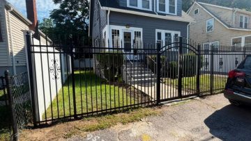 Black metal fence gate around a front walkway leading to a residential home